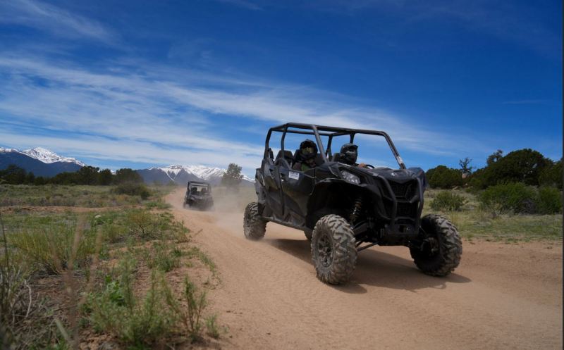Side-by-side UTV on a dusty open trail with Colorado mountains in the distance